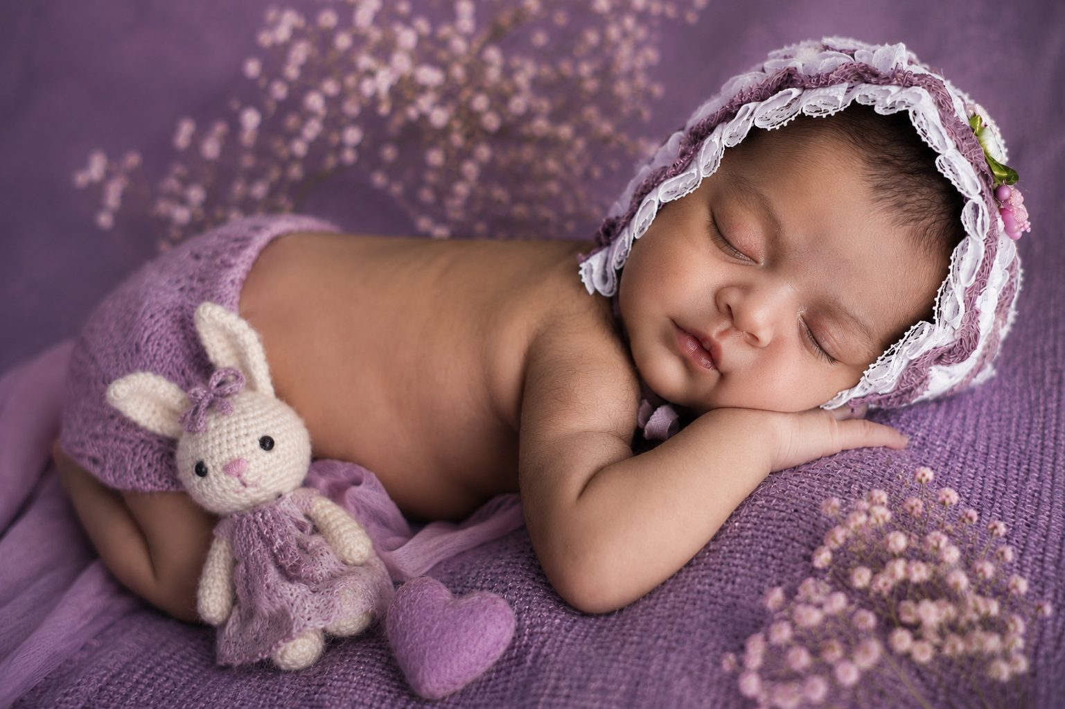 Sleeping newborn in a lace bonnet resting beside a crochet bunny toy