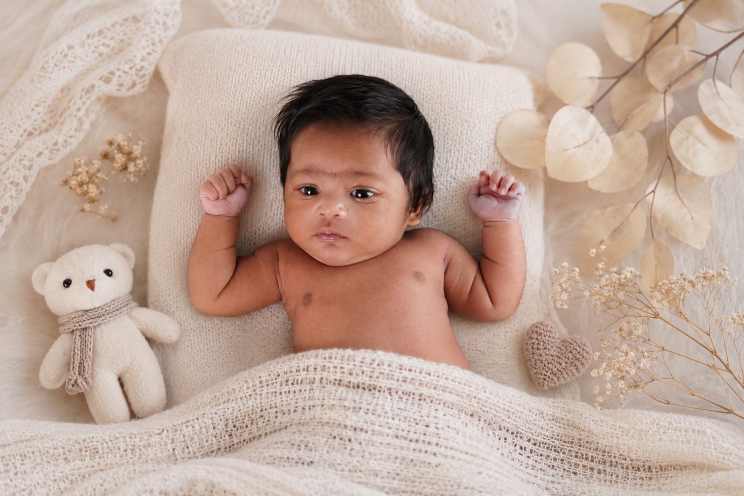 Baby swaddled in a soft yellow wrap inside a heart-shaped wooden bowl with dried florals
