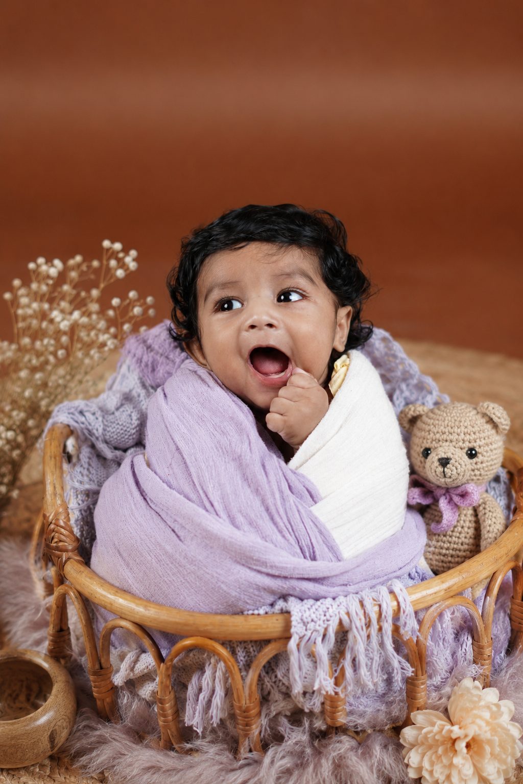 Newborn resting on a purple knit blanket surrounded by dried florals
